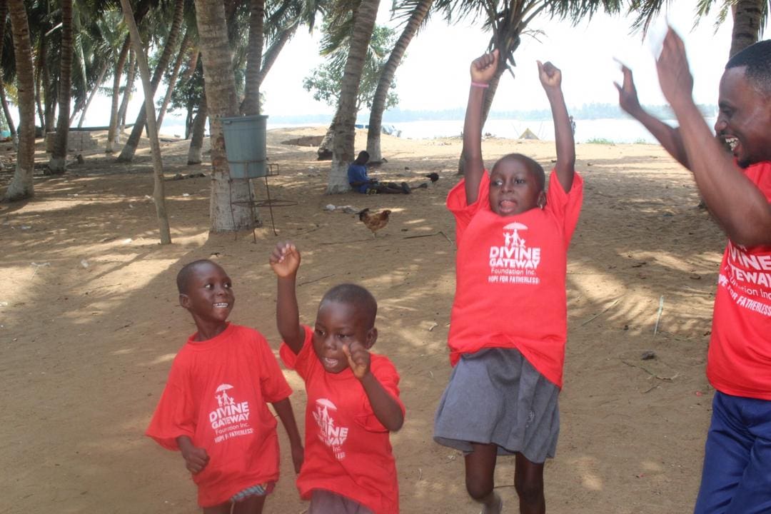 Three children are standing on the beach in red shirts.