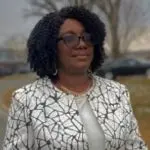 A woman in glasses and a jacket standing outside.