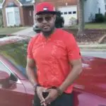 A man in red shirt standing next to a car.