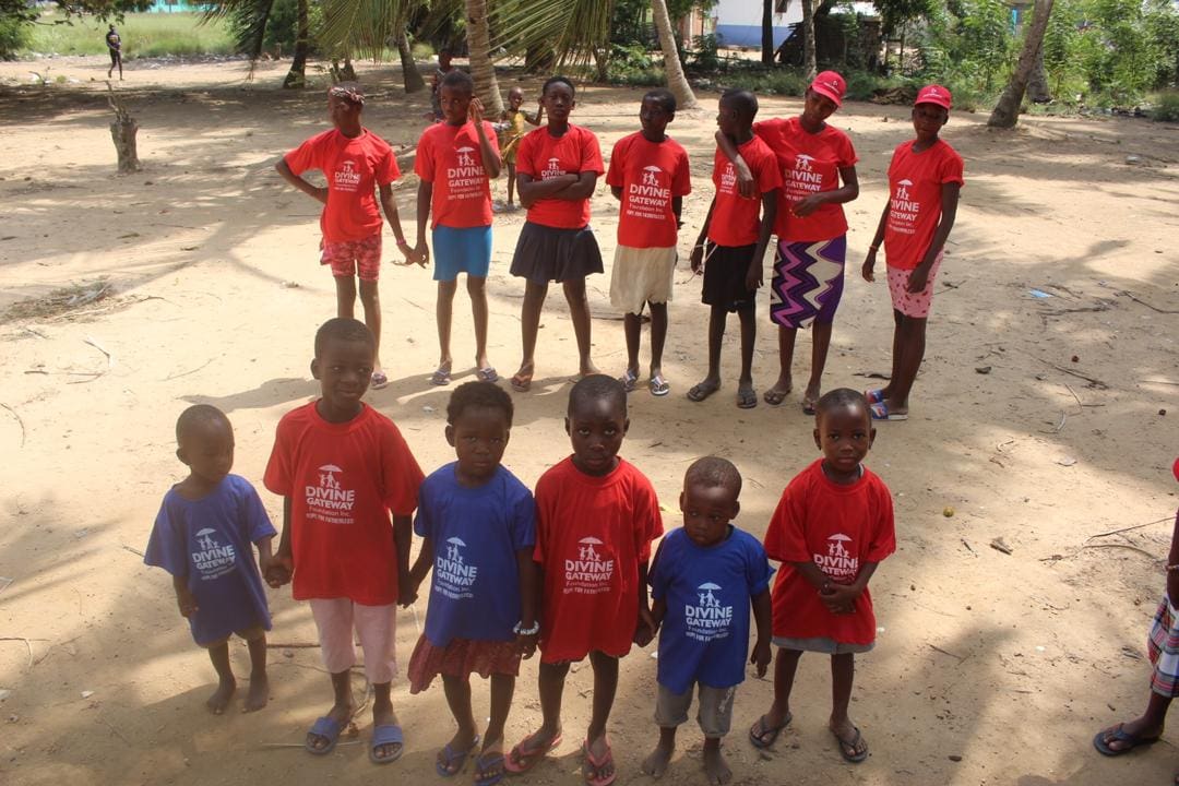 A group of children standing in the sand wearing red shirts.