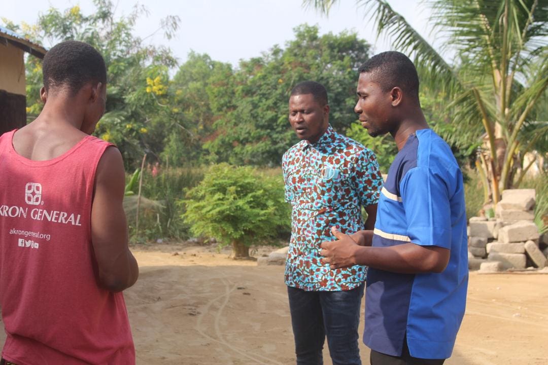 Three men standing in a field talking to each other.