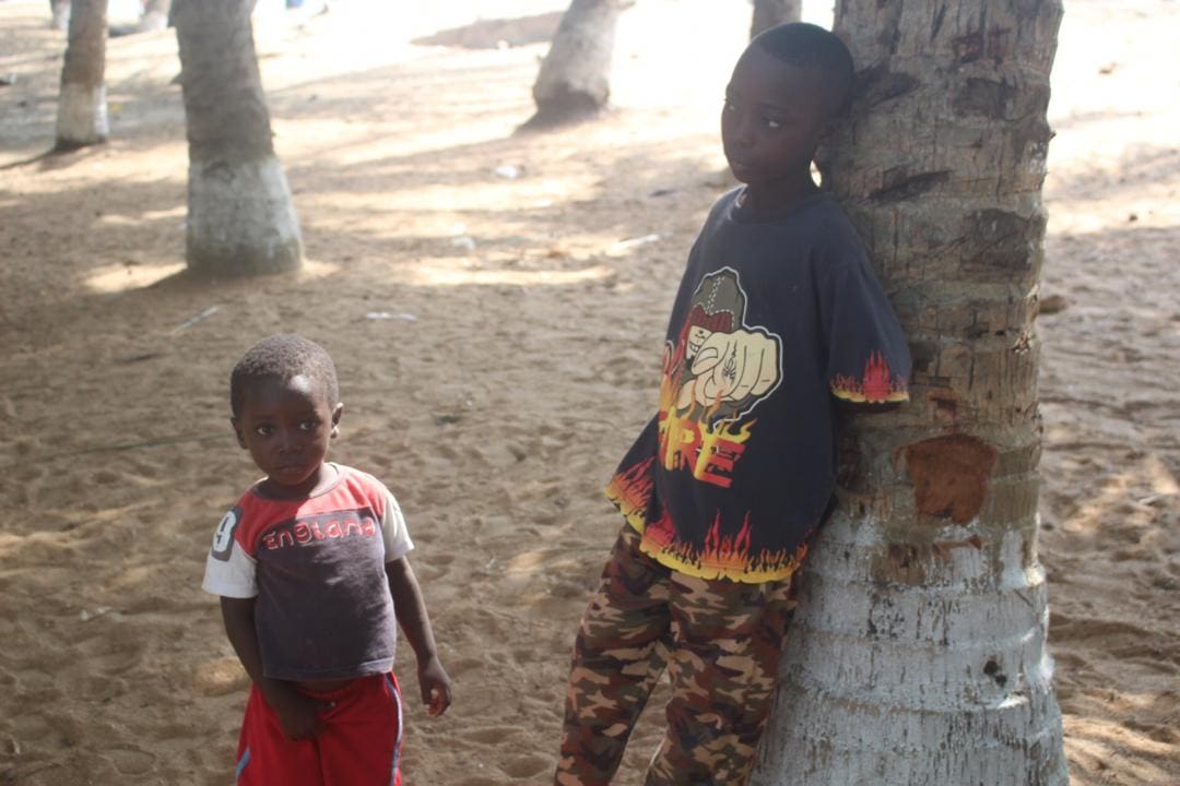 Two children standing next to a tree in the dirt.