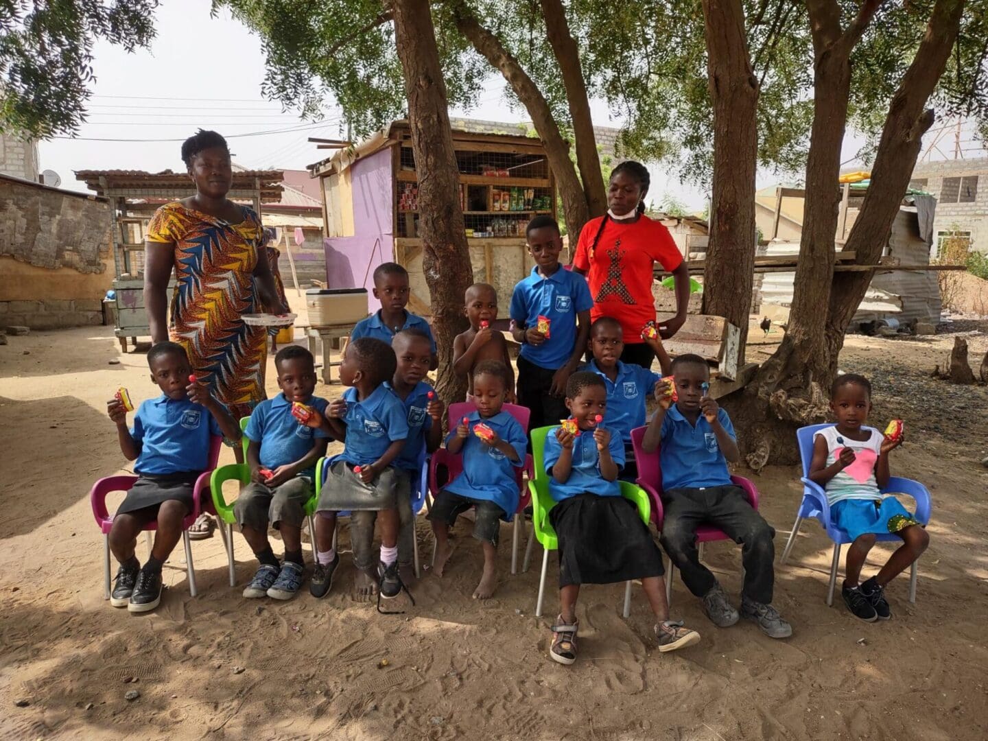 A group of children sitting in chairs under trees.