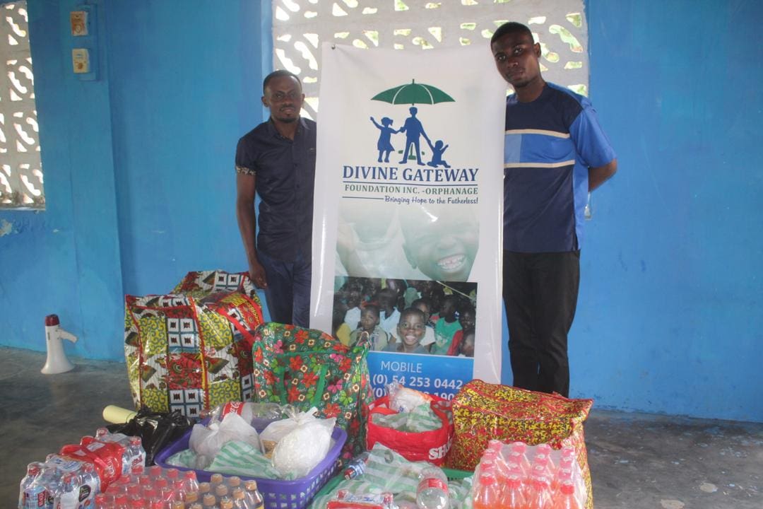 Two men standing next to a sign and some presents.